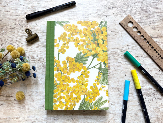 Bullet journal artisanal avec couverture motif mimosa posé sur un bureau