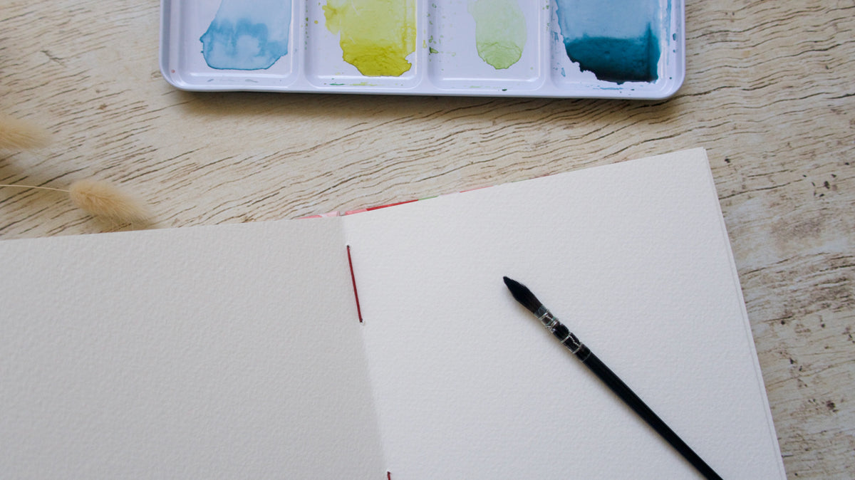 carnet d'aquarelle ouvert bien à plat, pinceau et palette d'aquarelle
